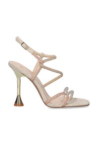 Sandalia de tacón alto con tiras nude adornadas con cristales, un tacón metálico dorado y una suela texturizada. Incluye una correa ajustable en el tobillo.