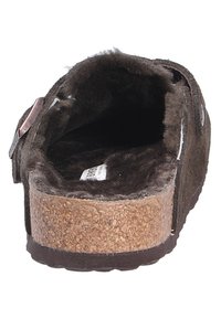Brown suède pantoffel met een zachte voering, kurken zool, verstelbare strap en een vlak ontwerp. Het binnenaanzicht toont de zachte textuur en de label.