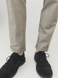 Pantalons beiges ajustés avec des revers, associés à des chaussures en daim bleu foncé. L'ensemble présente des chaussettes claires visibles au-dessus des chaussures.