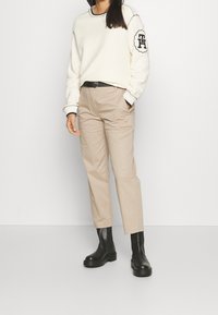 Kremowy sweter z czarnymi akcentami, beżowe spodnie i błyszczące czarne botki na kostkę. Spodnie mają prosty krój i boczne kieszenie.