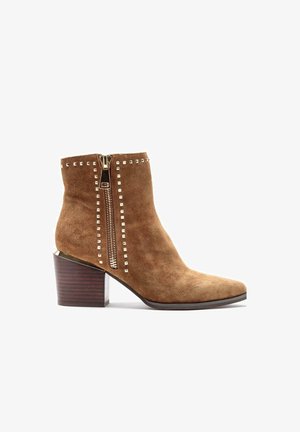 Braune Wildleder-Stiefelette mit spitzem Schuhkopf, goldener Reißverschluss und quadratischen Metallnieten entlang des Schafts, ausgestattet mit einem gestapelten Holzabsatz.