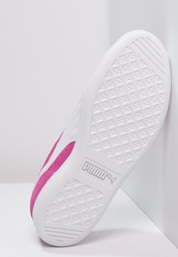 Baskets blanches et roses avec une semelle texturée, ornées d'un logo sur le côté. La tige combine des matériaux lisses et en daim.