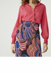 Rosa skjorta med knappar och långa, samlade ärmar, kombinerad med en mönstrad kjol med virvlande blå, rosa och svarta mönster.