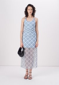 Blauw-wit geruite jurk met een getailleerde bustier en een doorschijnende rok, voorzien van spaghettibandjes en een zijsplit. Zwarte handtas en sandaaltjes met bandjes.