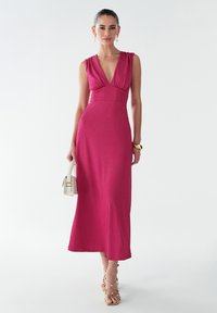 Fuchsia, sleeveless maxi dress with a V-neck and gathered shoulder detail. Smooth texture paired with strappy sandals and a small handbag.
