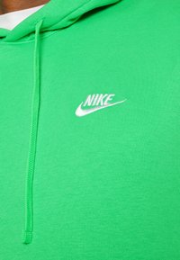 Grön Nike huvtröja med en vit broderad logotyp, snörhuv, ribbat mönster och slätt tyg.