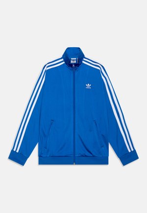 Veste de survêtement bleue en tissu lisse, dotée d'accents à trois bandes blanches sur les manches et de poches zippées sur le devant. Logo iconique sur la poitrine.