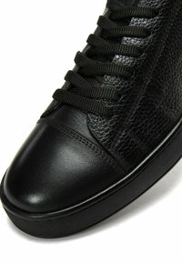 Sneaker in pelle nera con tomaia testurizzata, punta liscia e lacci neri piatti. Presenta una suola in gomma con un motivo discreto.