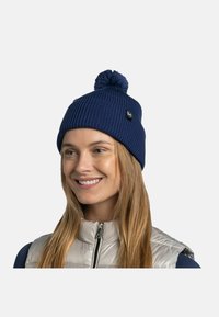 Navy ribbed beanie with a pom-pom top and logo patch. Made of knit material, it features a snug fit and textured surface.