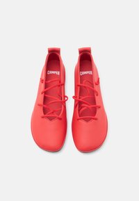 Red leather shoes with a smooth texture, rounded shape, and rounded toe. Features laces and a fabric loop at the back. Brand logo visible.