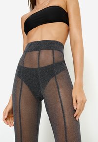 Μαύρα κολάν με ψηλόμεσο, διακοσμημένα με διάφανα πάνελ και λαμπερές ασημένιες ίνες, με ορθογώνιες περικοπές κατά μήκος των ποδιών.