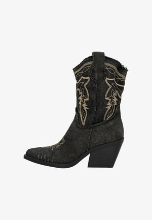Black denim ankle boot with a pointed toe, stacked heel, and intricate gold embroidery on the shaft. Distressed detailing along the toe.
