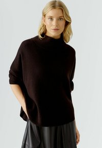 Schwarzer, oversize Strick-Turtleneck-Pullover mit umgeschlagenen Kanten, kurzen Ärmeln und entspannter Passform, kombiniert mit einem schwarzen Lederrock.