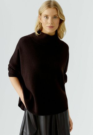 Zwart oversized gebreide coltrui met omgeslagen randen, korte mouwen en een relaxte pasvorm, gecombineerd met een zwarte leren rok.