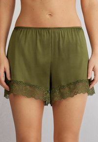 Olivgröna shorts i ett mjukt tyg, med en vågig spetskant i nederkant. Elastisk midja för komfort.