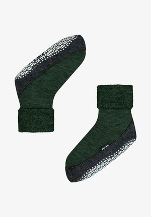 Calzini verdi con un polsino spesso e texturizzato e una suola in gomma grigia scura, decorata con un motivo. L'etichetta del marchio "FALKE" è visibile sul lato.