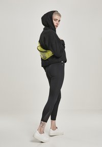 Felpa nera con cappuccio e cordoncino, leggings neri, sneakers bianche e una cintura traslucida verde. Ritagli notevoli sulle gambe vicino alle caviglie.