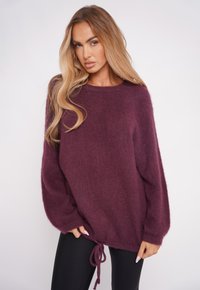 Burgundowy, oversize sweter dziany z długimi rękawami, o miękkiej teksturze i ściągaczu u dołu, pozwalającym na regulację dopasowania.