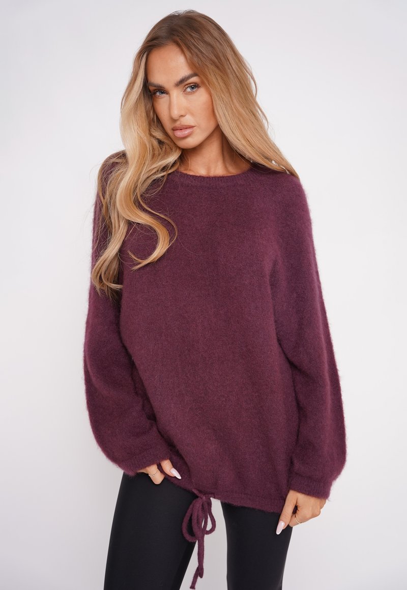 Burgundowy, oversize sweter dziany z długimi rękawami, o miękkiej teksturze i ściągaczu u dołu, pozwalającym na regulację dopasowania.