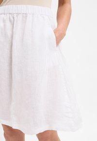 Valkoinen pellavasekoitekangas hame, jossa on joustava vyötärö, sivutaskut ja lentävä siluetti. Hieman läpinäkyvä, sileä tekstuuri ja polven mittainen.