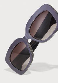 Lilla oversized solbriller med mat finish og mørke gradient linser. Tekstureret sort og grå accentside. Firkantede stel.