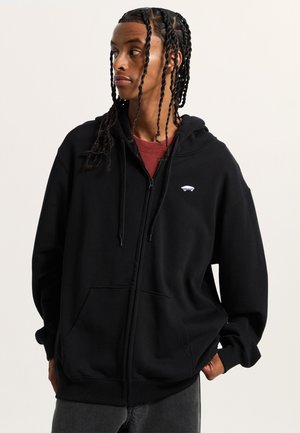 Black zip-up hoodie made of soft fabric, featuring a front pocket and a small white graphic on the chest. Hood with drawstrings.