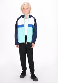 Lys blå og marineblå hættetrøje med hvide og blå striber; parret med sorte bukser og sorte sneakers. Minimalistisk design og pasform.