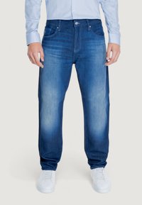 Pantaloni in denim blu con vestibilità comoda, texture sbiadita, cinque tasche e chiusura con bottone, abbinati a sneaker bianche.