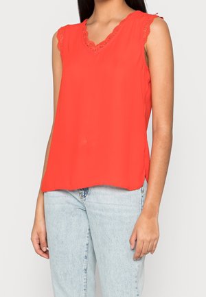 Rød ærmeløs bluse med V-hals, prydet med blondetrim langs halsudskæringen og skuldrene. Fremstillet af letvægtsstof, lige kant nederst.