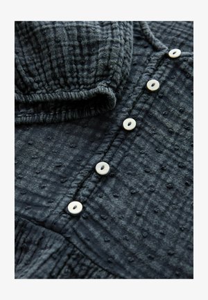 Vêtement texturé bleu foncé avec un design à boutons, comportant cinq boutons de couleur claire et un tissu doux et froissé.