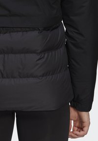 Black insulated jacket with a smooth upper section and puffy lower section, featuring a slightly shiny texture and elastic cuffs.