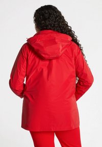 Röd vattentät jacka med huva, långa ärmar och rak passform. Slät textur och minimal detaljering på baksidan.