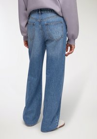 Jeans a vita alta, blu chiaro e a gamba larga, con due tasche posteriori e una texture sbiadita, abbinati a un felpa grigia di taglio ampio.