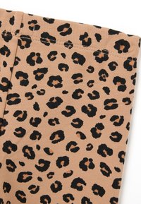 Luipaardprintstof in bruin met zwarte en bruine vlekken. Zachte textuur met zichtbare stiksels langs de rand. Ontwerp is uniform en patroonmatig.