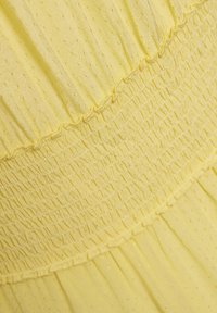 Abito giallo con un tessuto testurizzato, caratterizzato da dettagli arricciati e un design a strati. Materiale morbido e leggero con una leggera lucentezza.