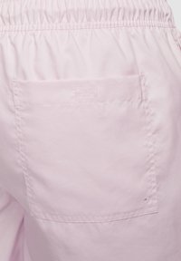 Shorts rose clair avec une taille élastique et une poche arrière. Texture lisse avec un minimum de détails de couture.