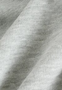 Tessuto di maglia grigio chiaro con una consistenza morbida, che presenta leggere variazioni di tonalità e un motivo a trama diagonale.