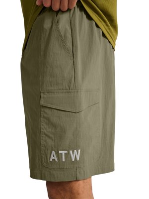 Licht olijfgroene cargoshorts met een klepzak geborduurd met "ATW", gedragen door een persoon met de hand rustend op de heup.