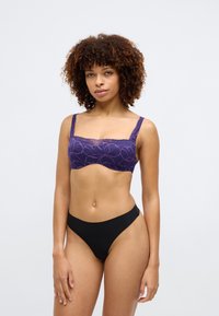 Violets žakarda bralette ar ziedu rakstu, plato siksniņu un viļņotām malām, kopā ar melniem augstās jostasvietas apakšbiksēm. Gluda tekstūra.