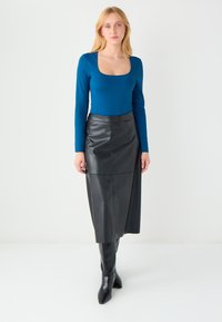 Bluzka z długim rękawem i kwadratowym dekoltem w niebieskim materiale, zestawiona z czarną skórzaną ołówkową spódnicą. Gładka faktura, długość do kolan, dopasowany krój.