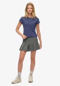 Camiseta de manga corta azul marino combinada con una falda plisada a rayas grises. La modelo lleva zapatillas beige y calcetines a rayas.