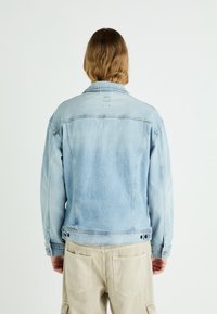 Svetlo modra denim jakna z ravnim krojem, klasičnim ovratnikom in gumbnimi zapiranji. Ima nazaj šiv in podrobnosti šivanja.