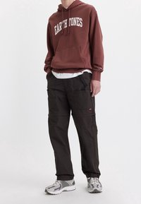 Bordová mikina s potiskem "ZEMSKÉ TONY", klokanka, kombinováno s tmavými cargo kalhotami s bočními kapsami a černými akcenty, obuta s šedými teniskami.