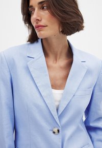 Ljusblå blazer med en strukturerad design, notch-lapel, enknappsstängning och bröstficka, gjord av texturerat tyg.