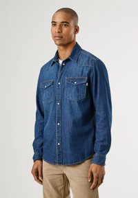Blauwe denim shirt met een puntkraag, twee borstzakken en knoopsluitingen. Heeft contrasterende stiksels en lange mouwen.