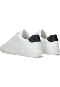 White leather sneakers with a contrasting black heel tab, flat rubber soles, and minimalistic design. Stitching details along the sides.