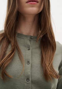 Cardigan verde oliva con scollo rotondo, caratterizzato da cinque bottoni scuri lungo la parte anteriore e una texture morbida e a maglia fine.