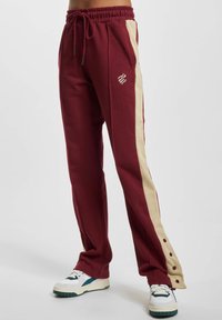 Bordeaux sweatpants med beige sidelister, der har en elastisk talje, snoretræk og trykknapdetaljer ned langs benet.