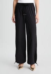 Pantaloni sportivi neri con vestibilità rilassata, dotati di pannelli laterali in rete, vita elastica e lacci regolabili alle caviglie.