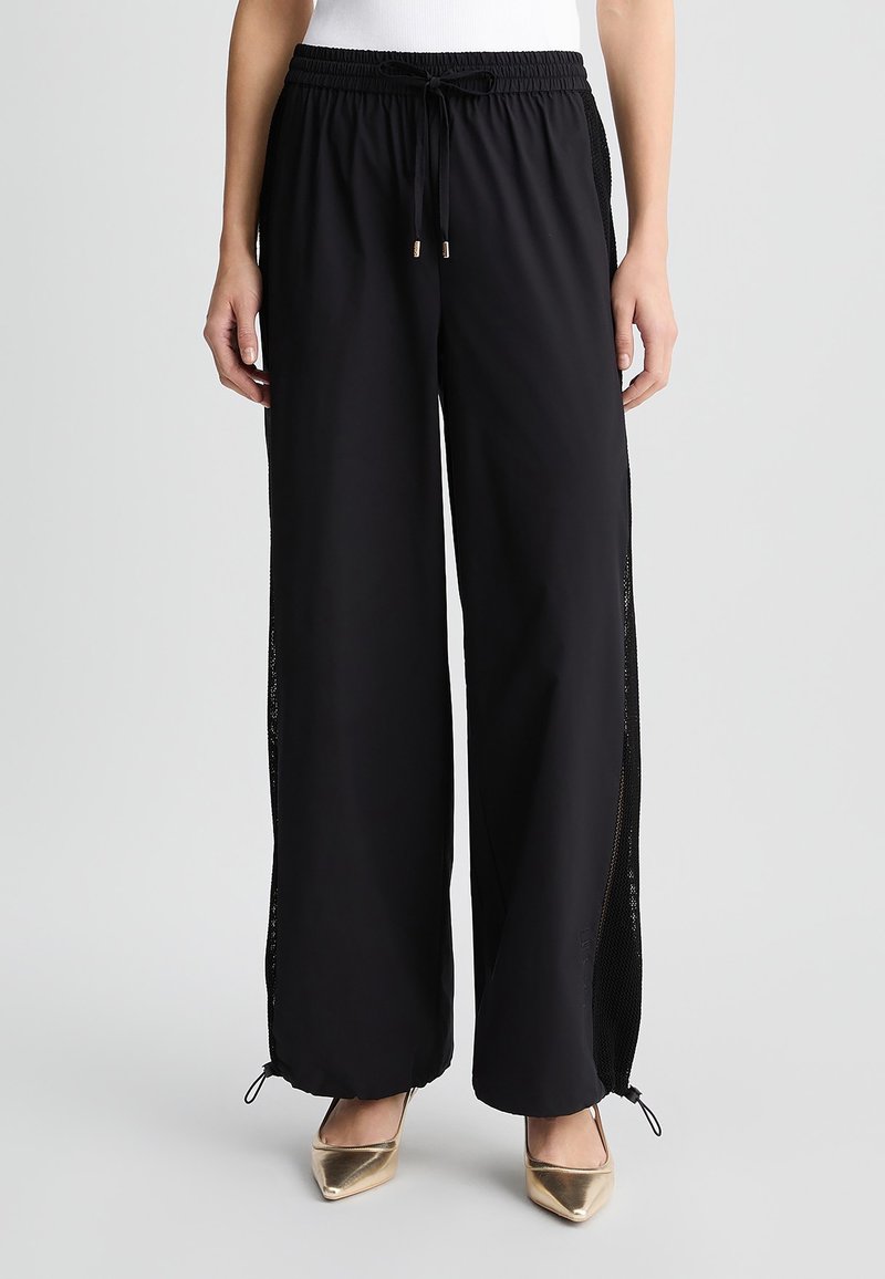 Pantaloni sportivi neri con vestibilità rilassata, dotati di pannelli laterali in rete, vita elastica e lacci regolabili alle caviglie.